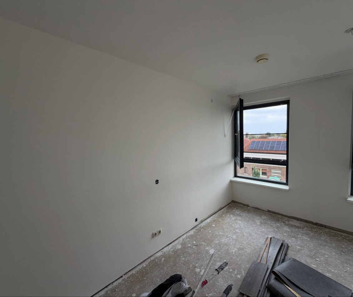 Kamer met strak gestucte witte wanden en plafond en twee openstaande ramen