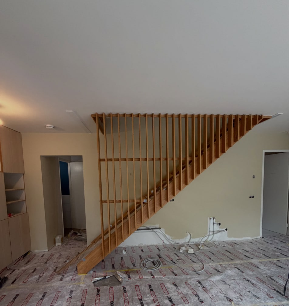 Woonkamer met gespoten wanden en plafond en een open houten trap, de vloer nog afgedekt